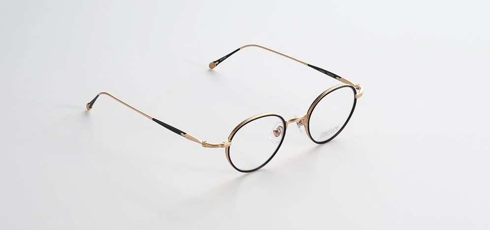 A pair of Matsuda gold-framed round eyeglasses with black temple tips on a white background.