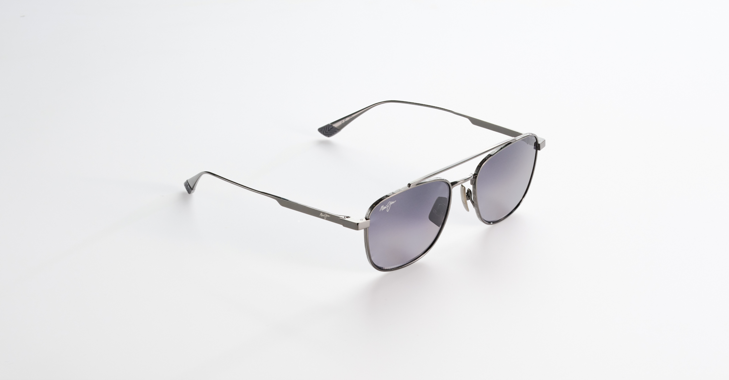 A pair of silver-framed Maui Jim sunglasses with dark tinted lenses lying on a white surface.