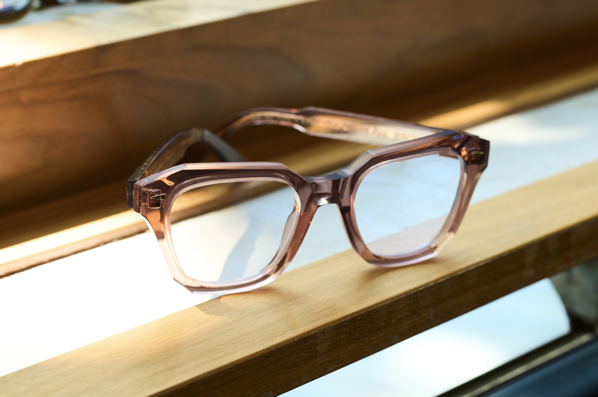 Pink and clear plastic eyeglasses resting on a wooden surface.