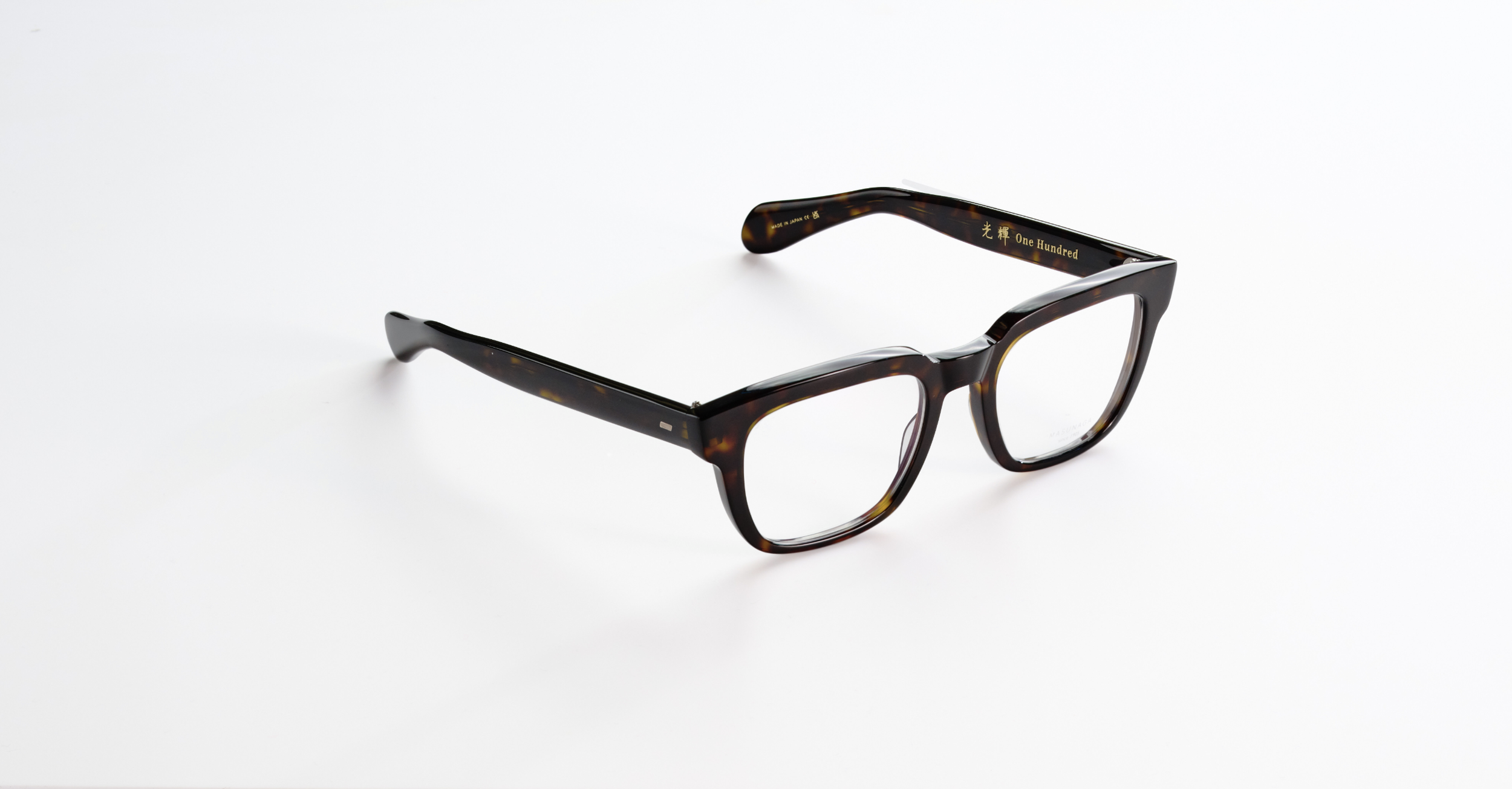 A pair of Masunaga tortoise shell eyeglasses with gold lettering on the arm, placed on a white surface.