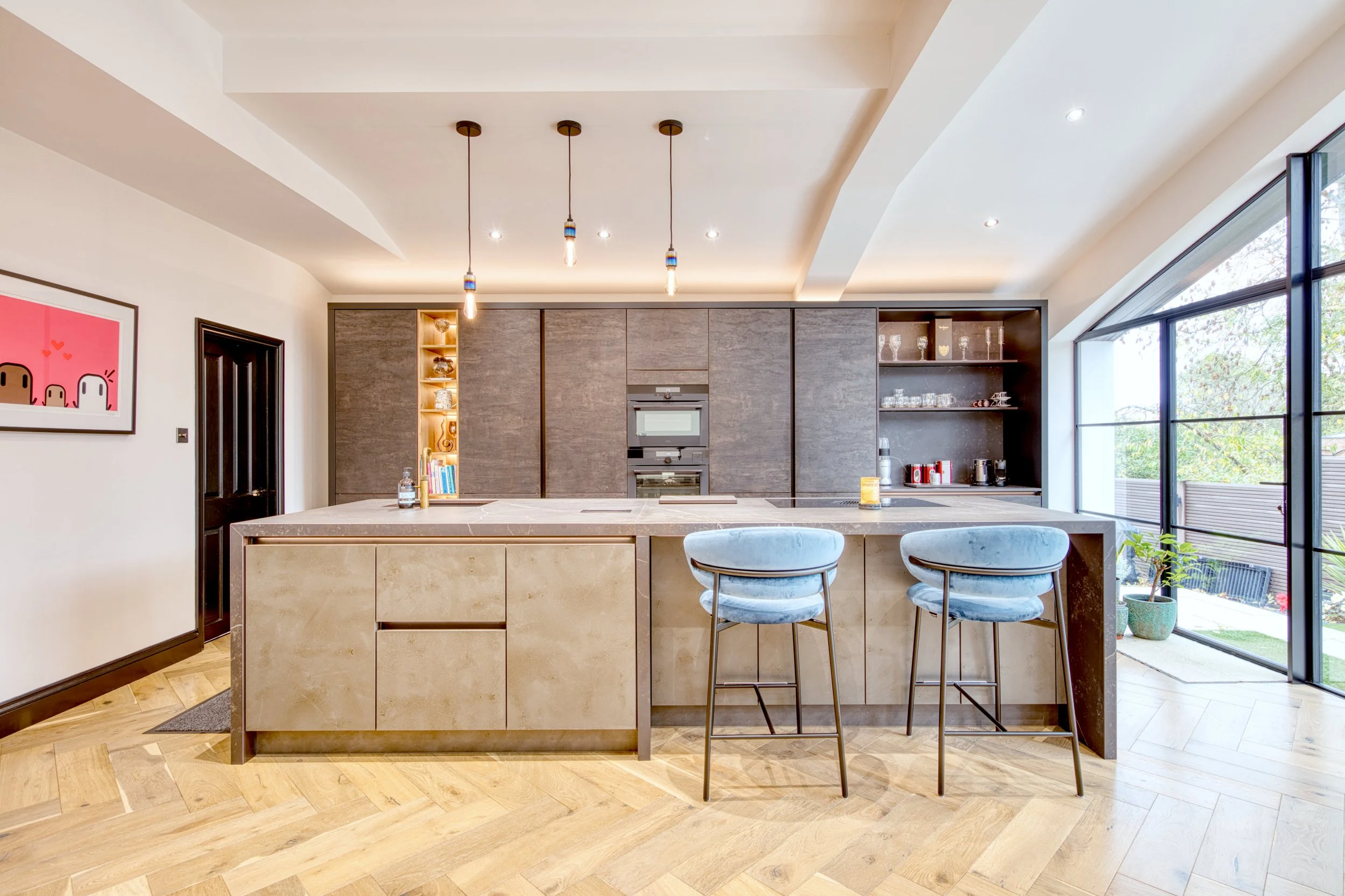 Modern kitchen with a large island, dark cabinets, open shelving, pendant lighting, large windows, and hardwood flooring.