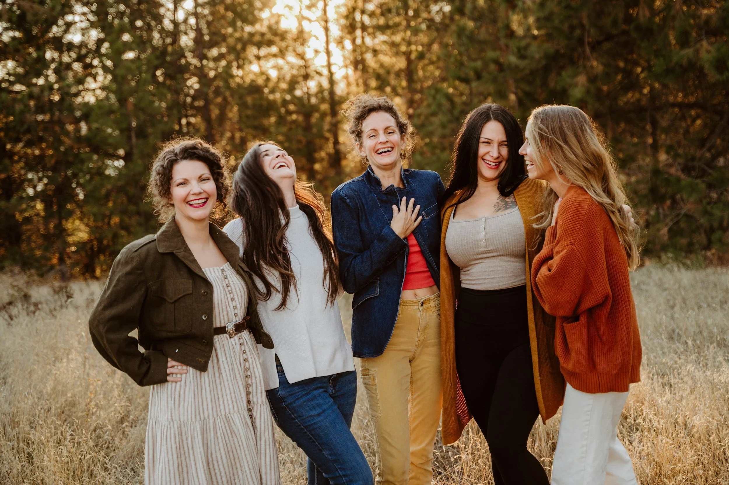 Five women laughing and enjoying each other's company outdoors during sunset.