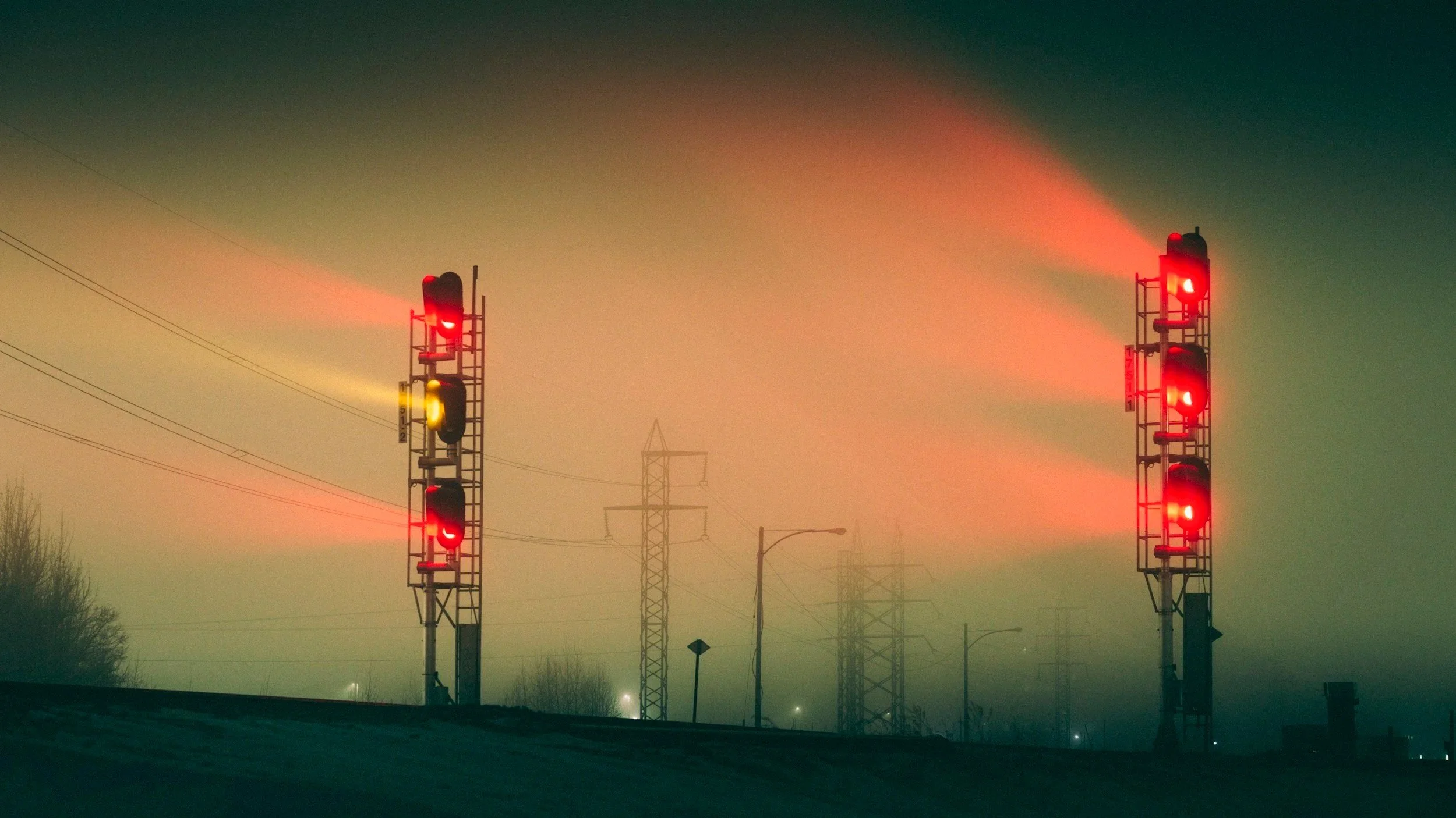 signal lights burn through fog with power towers in hazy background