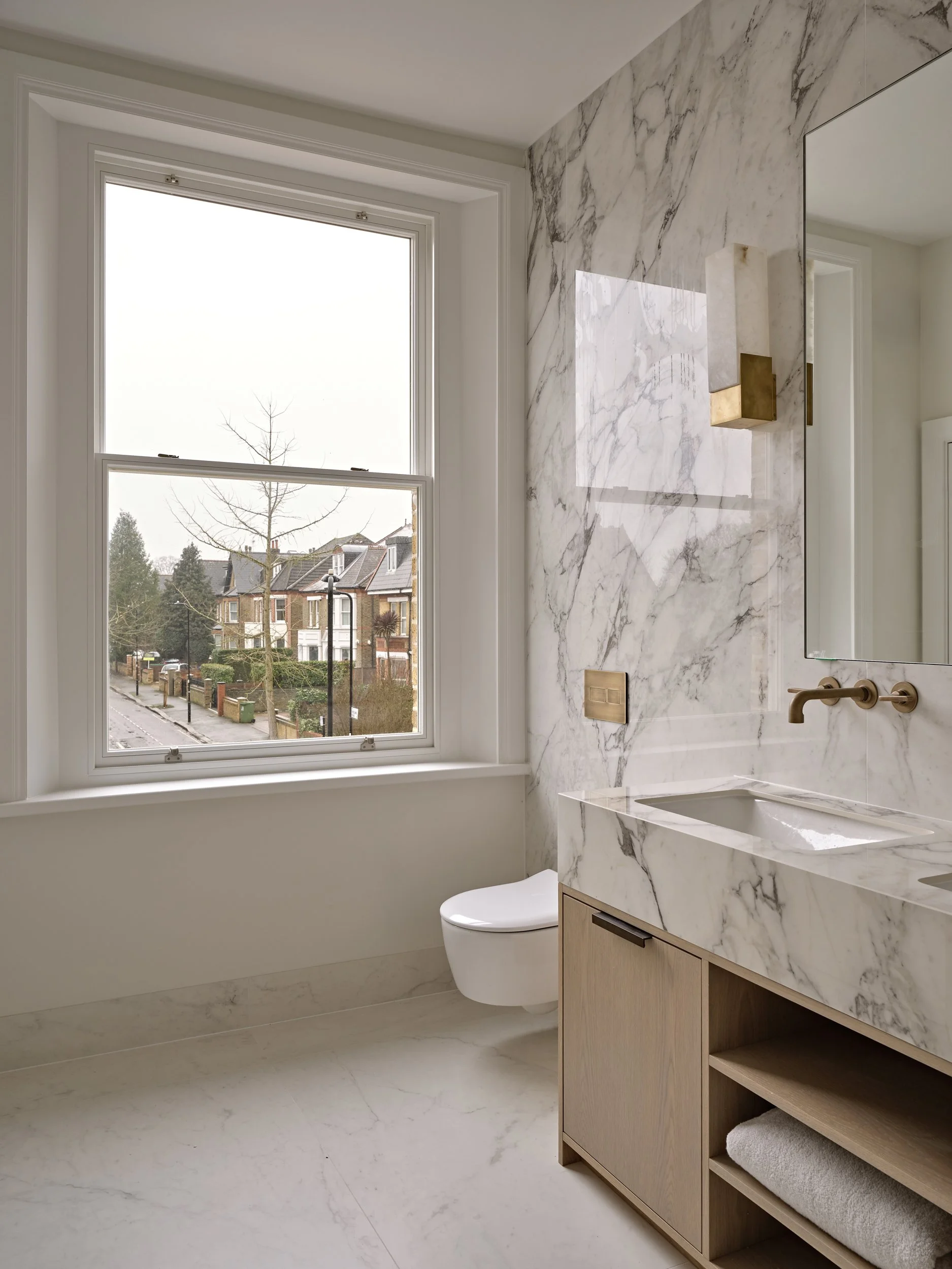 Modern bathroom with large window, marble walls, a wooden vanity with a marble countertop, a built-in sink, and a wall-mounted faucet.