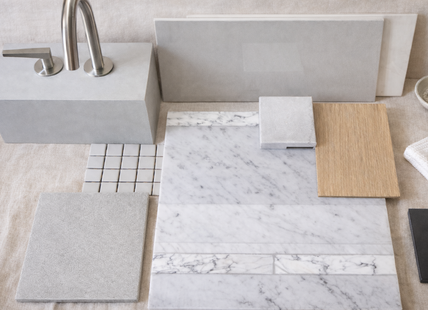 Arrangement of various tile samples including marble, wood, stone, and ceramic displayed on a beige surface.