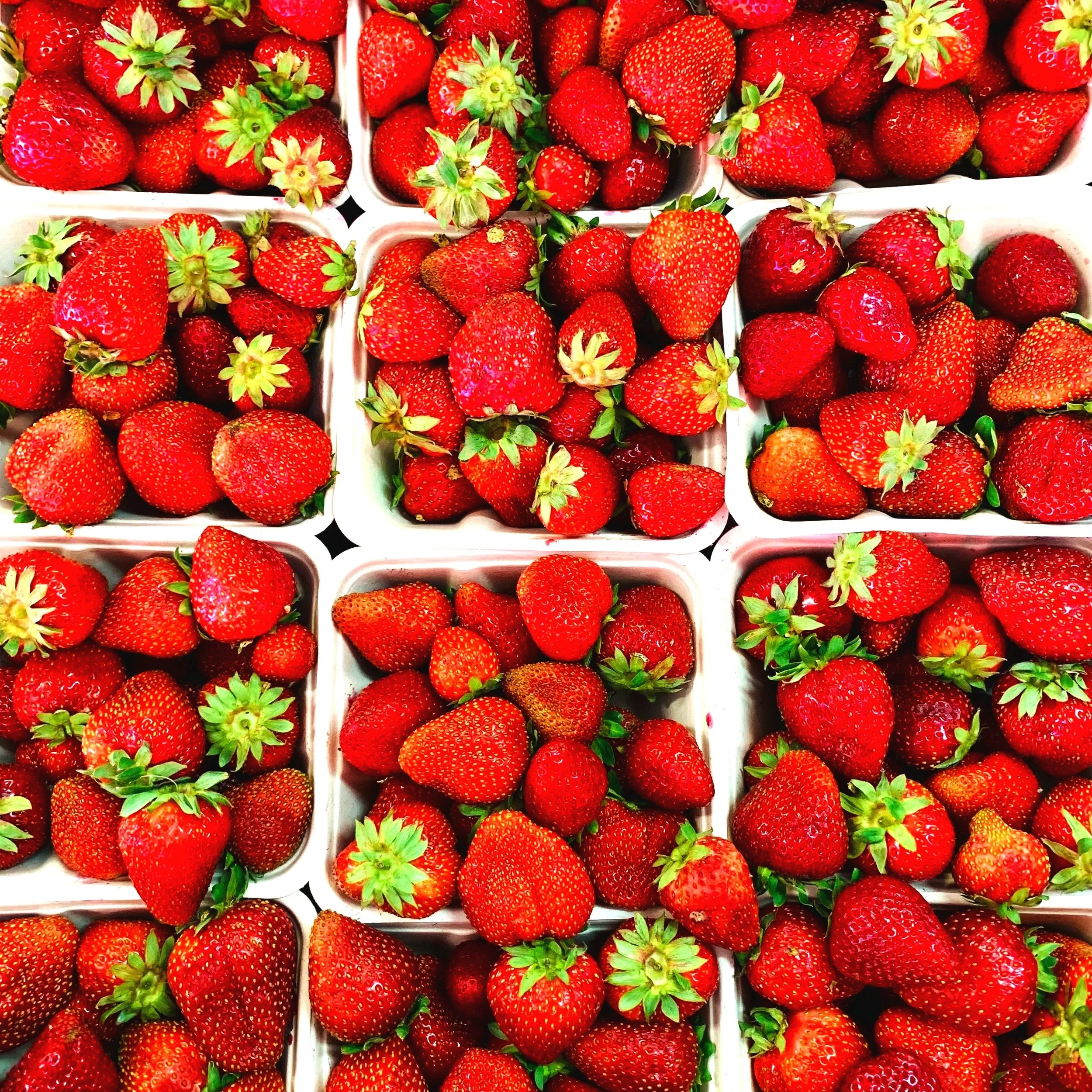 Close-up of fresh red strawberries with green leaves, displayed in white trays.