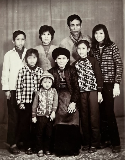 Photograph of a multi-generational Asian family with seven members, including adults and children, posed in front of a plain backdrop.