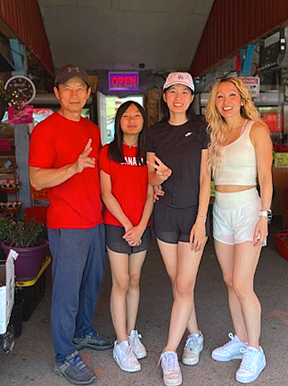 Four people standing in front of a storefront with a neon 'OPEN' sign visible behind them. They are smiling and dressed casually.