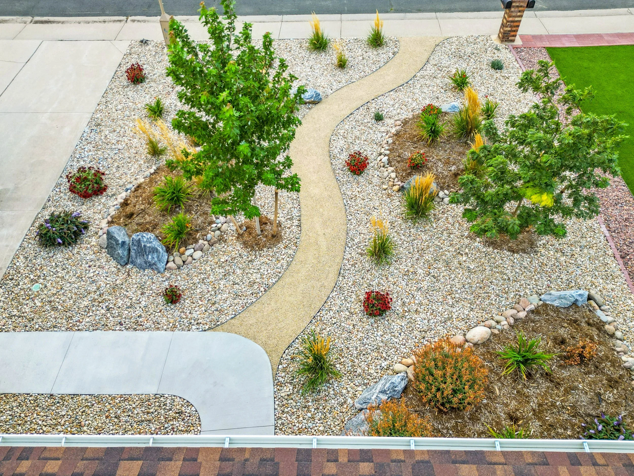 A landscaped front yard with a pathway, trees, bushes, and decorative rocks.
