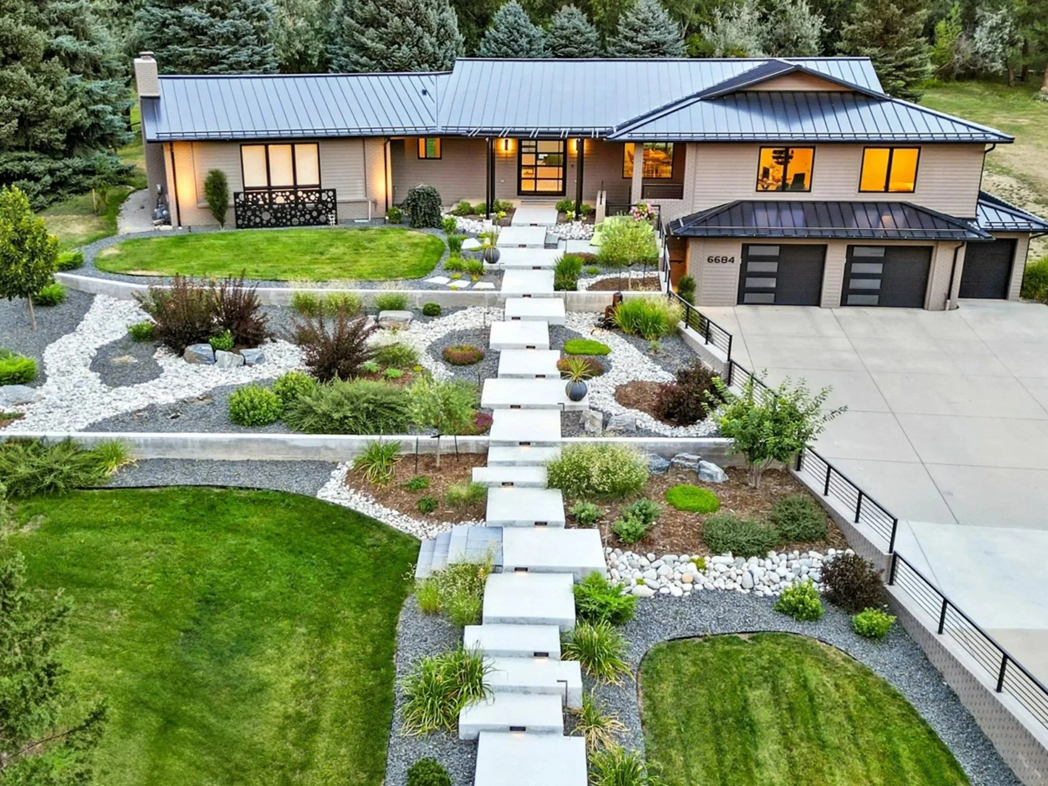 Front yard view of a modern house with a landscaped garden, lawn, and concrete pathway in a suburban setting.