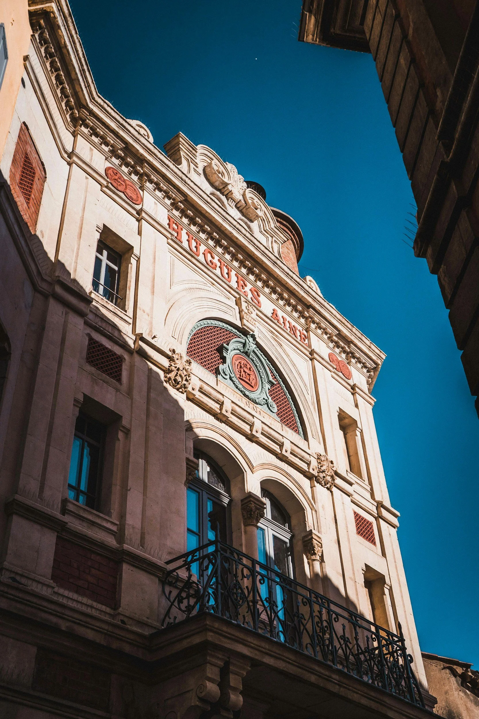 Upside-down view of a historic building with ornate architecture, large windows, and a decorative balcony, under a clear blue sky with a small white dot.