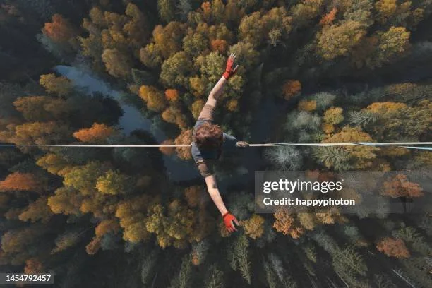 A person crossing a high ropes course over a forest with autumn-colored trees, wearing a harness and gloves.