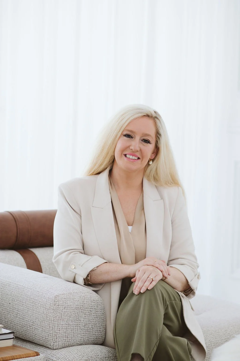 Photo of Embodied Leadership Group, LLC founder smiling while seated on a beige couch in a bright, natural-light room with white curtains.