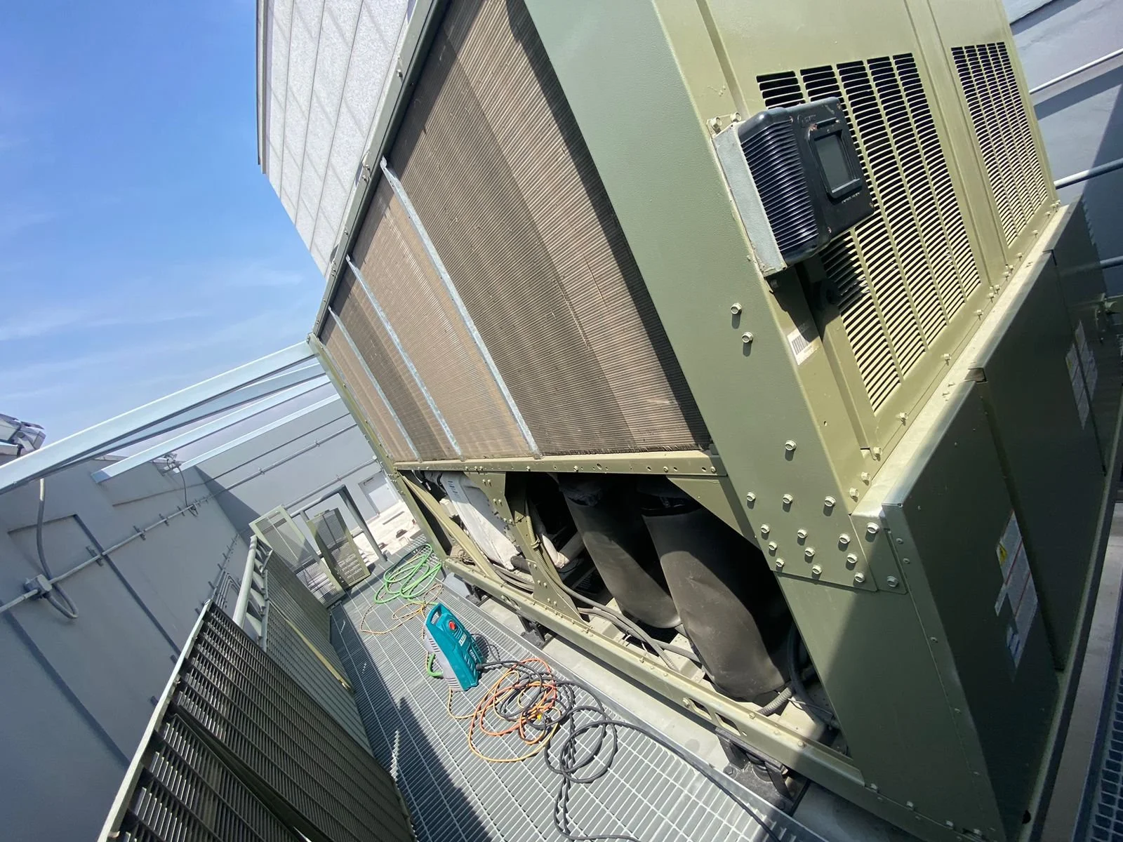 Un aire acondicionado grande y verde en una azotea, con cables y equipos de mantenimiento