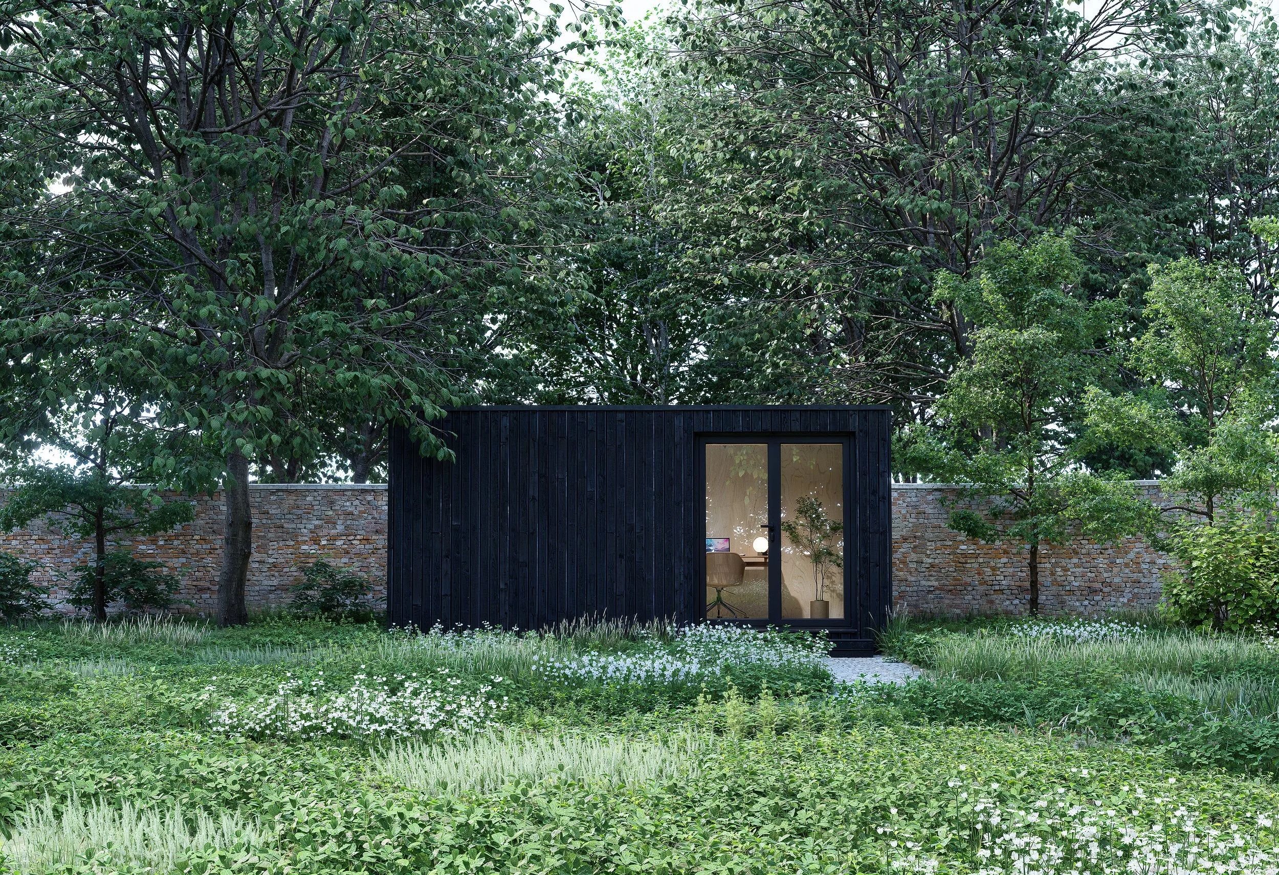 A small black wooden shed or tiny house with a glass door, surrounded by lush greenery and trees, with a brick wall in the background and wildflowers and grass in the foreground.