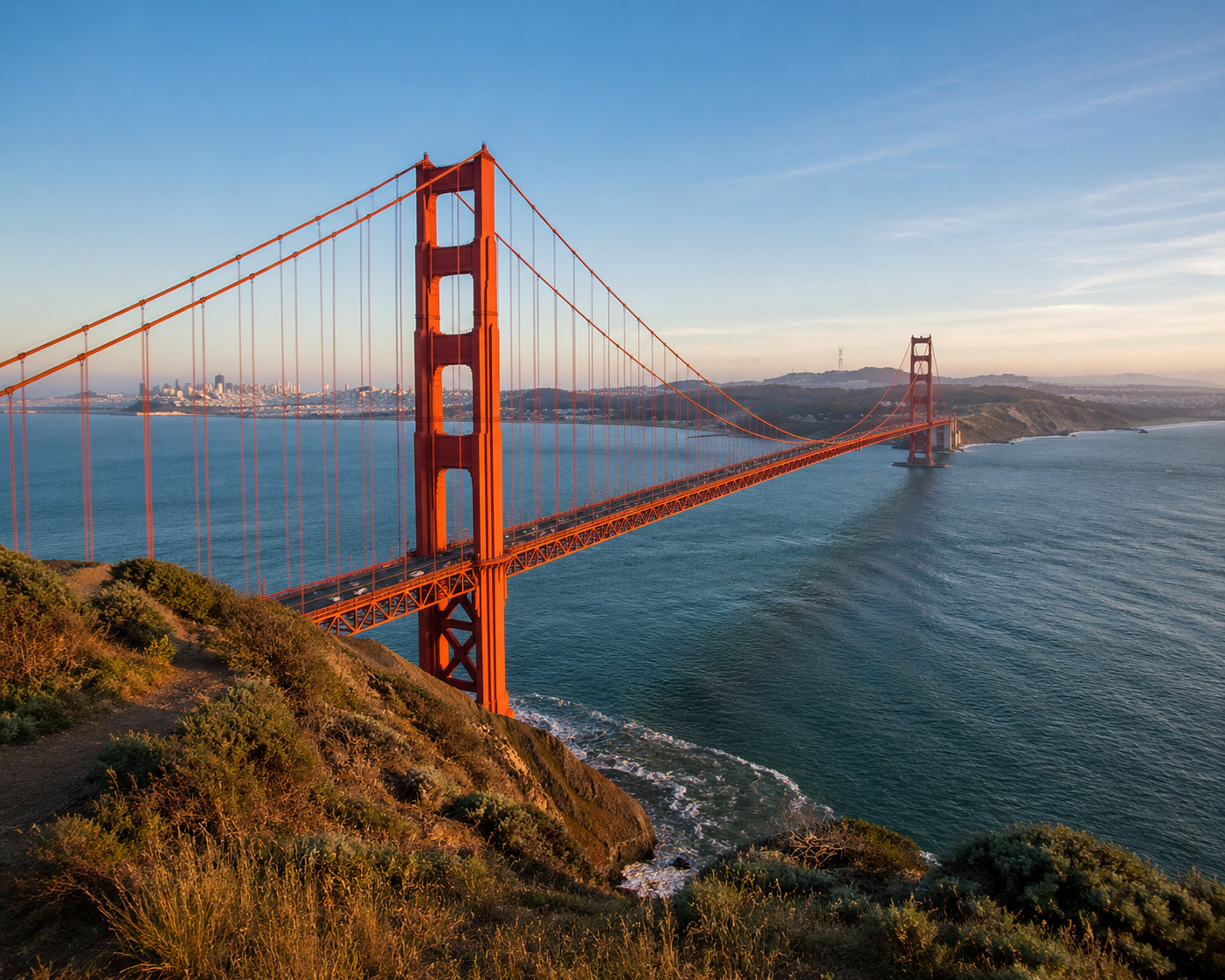 Golden Gate Bridge spanning the water with city skyline in the distance under a partly cloudy sky.