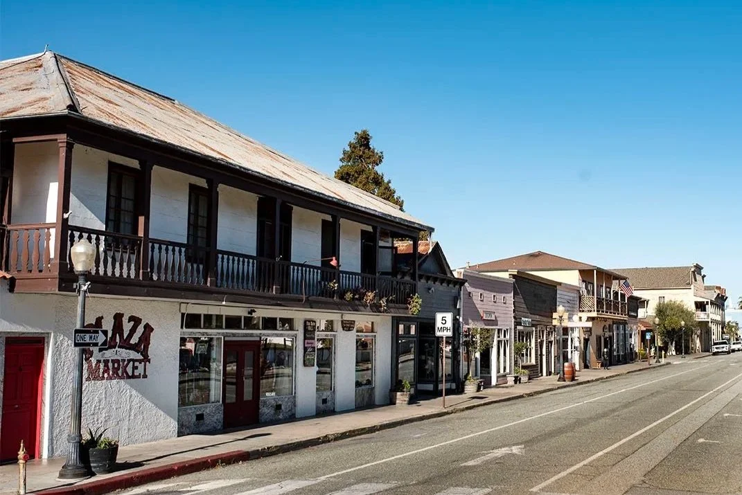 Street view of a small town with shops and apartments, clear sky, no people visible.