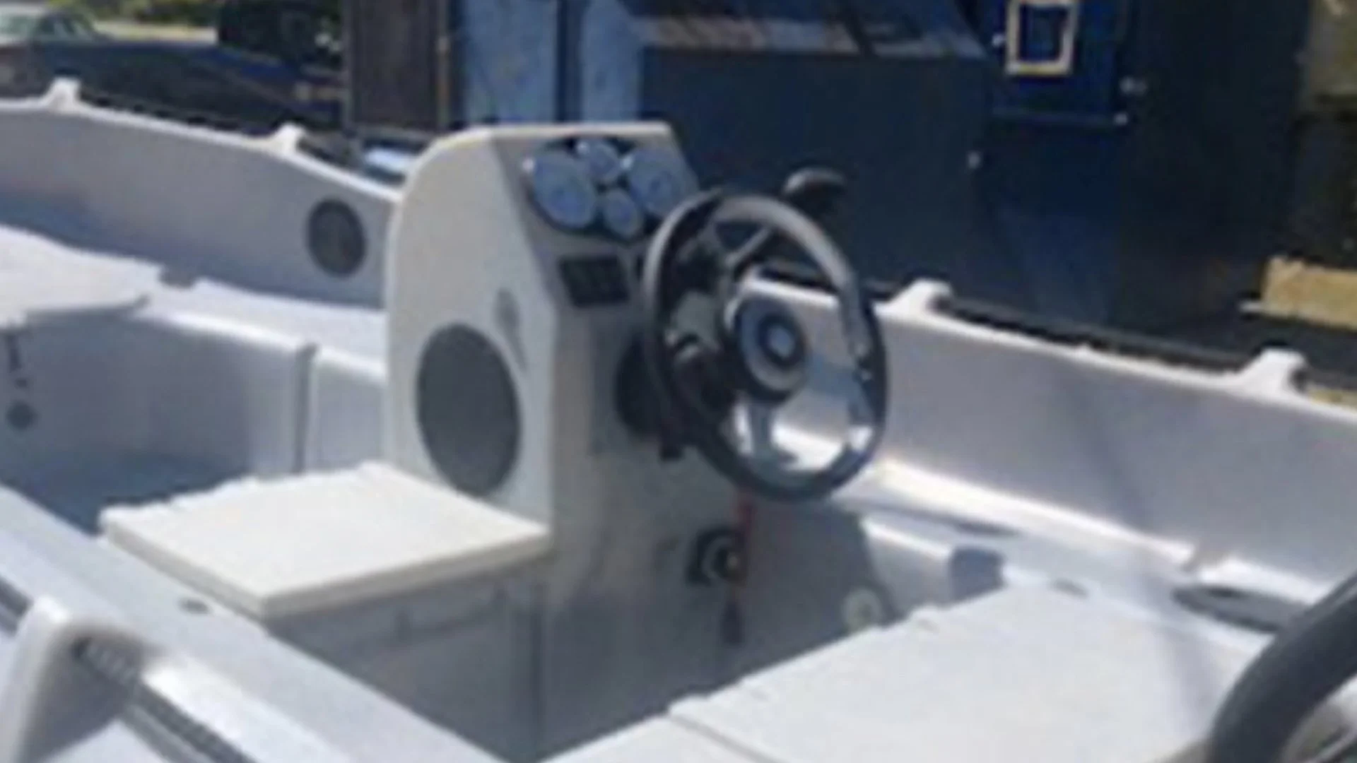The image shows the steering wheel and dashboard of a small boat with a white interior.
