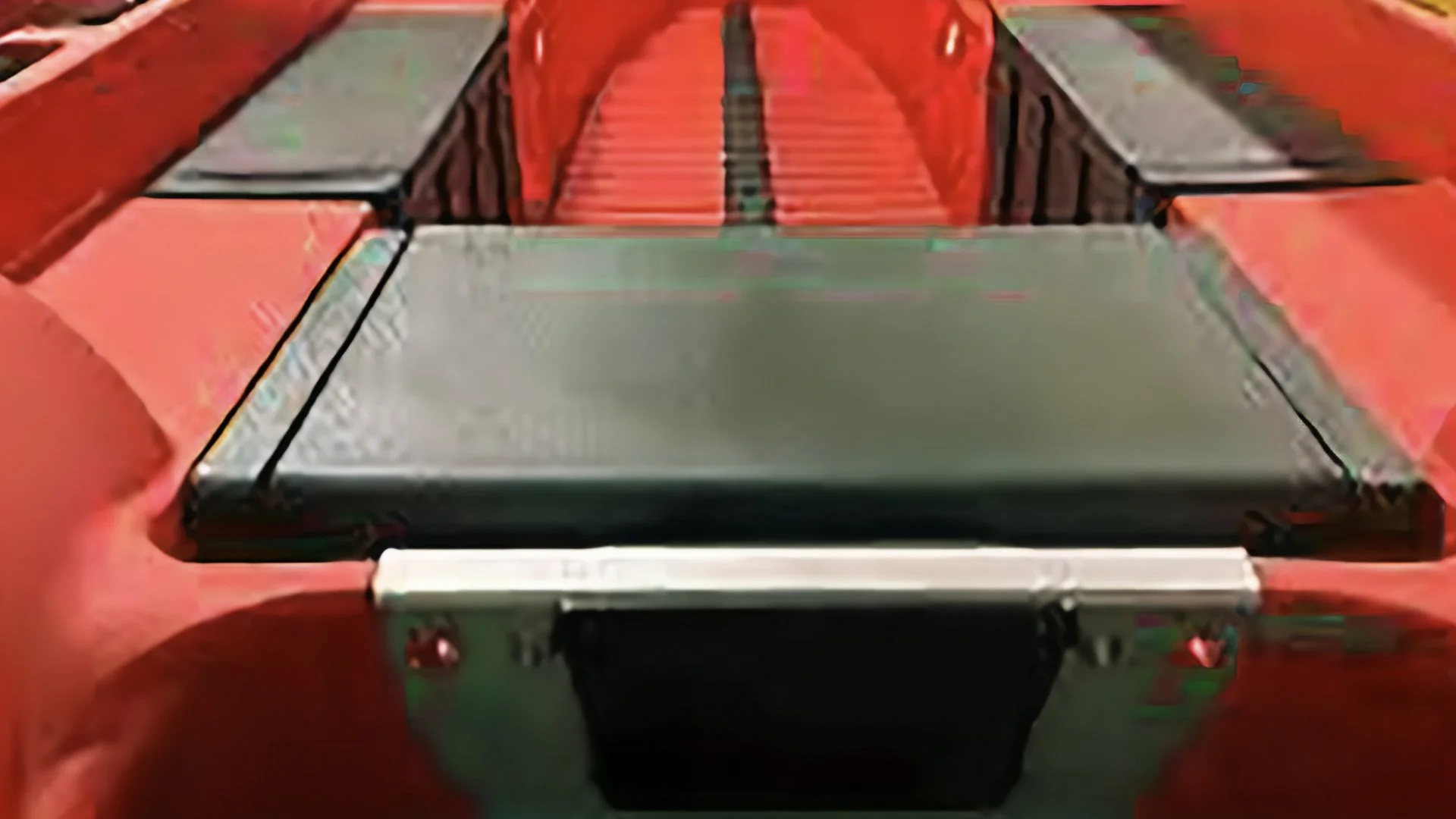 Close-up of a red object with a silver metallic component in the foreground, possibly part of a mechanical or electronic device.