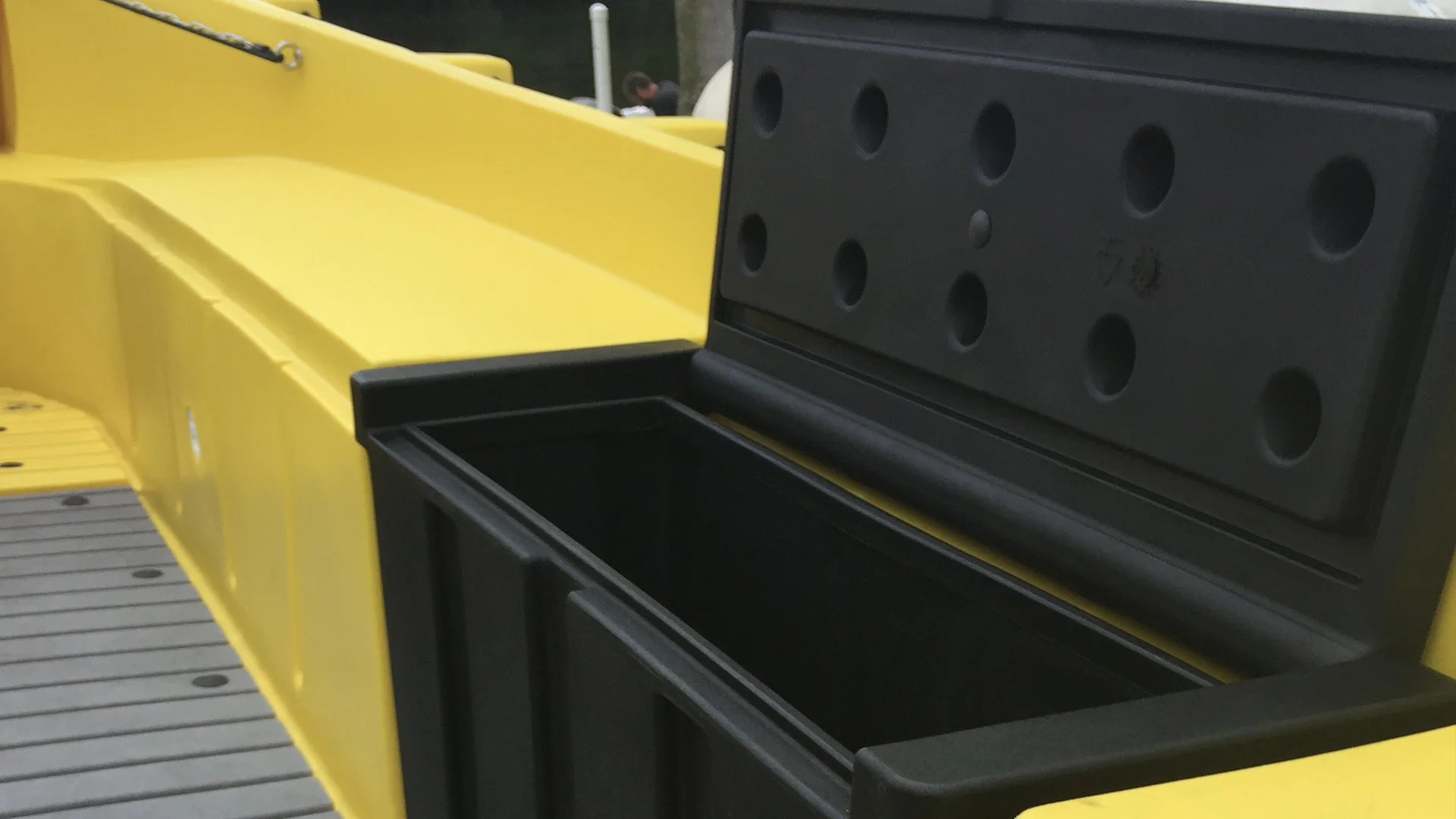 Close-up of a yellow boat with an open storage compartment showing a black lid and empty interior.