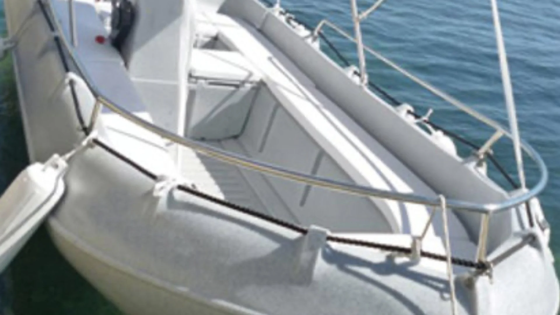 Close-up view of a white sailboat with railings and rigging, docked on calm water.