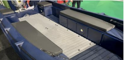 Close-up of a boat with a blue exterior and gray interior, featuring a foldable seat and a flat surface for storage or seating.