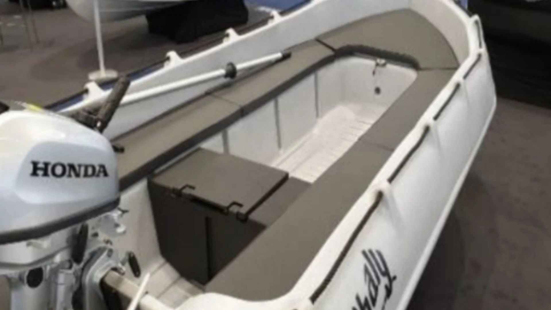 Small white and gray motorboat with Honda outboard engine, gray seating, and storage compartment, displayed indoors.