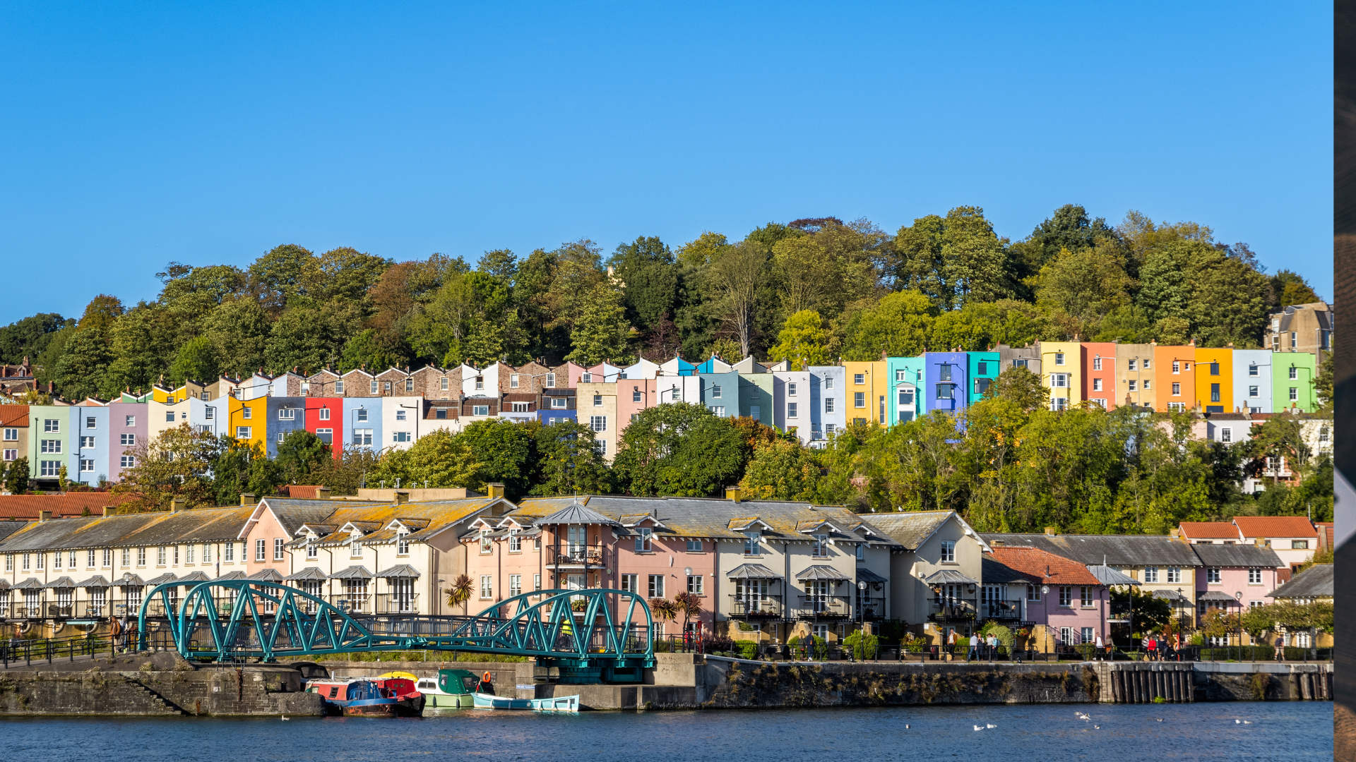 Colorful houses on a hillside with water and boats in the foreground and a clear blue sky