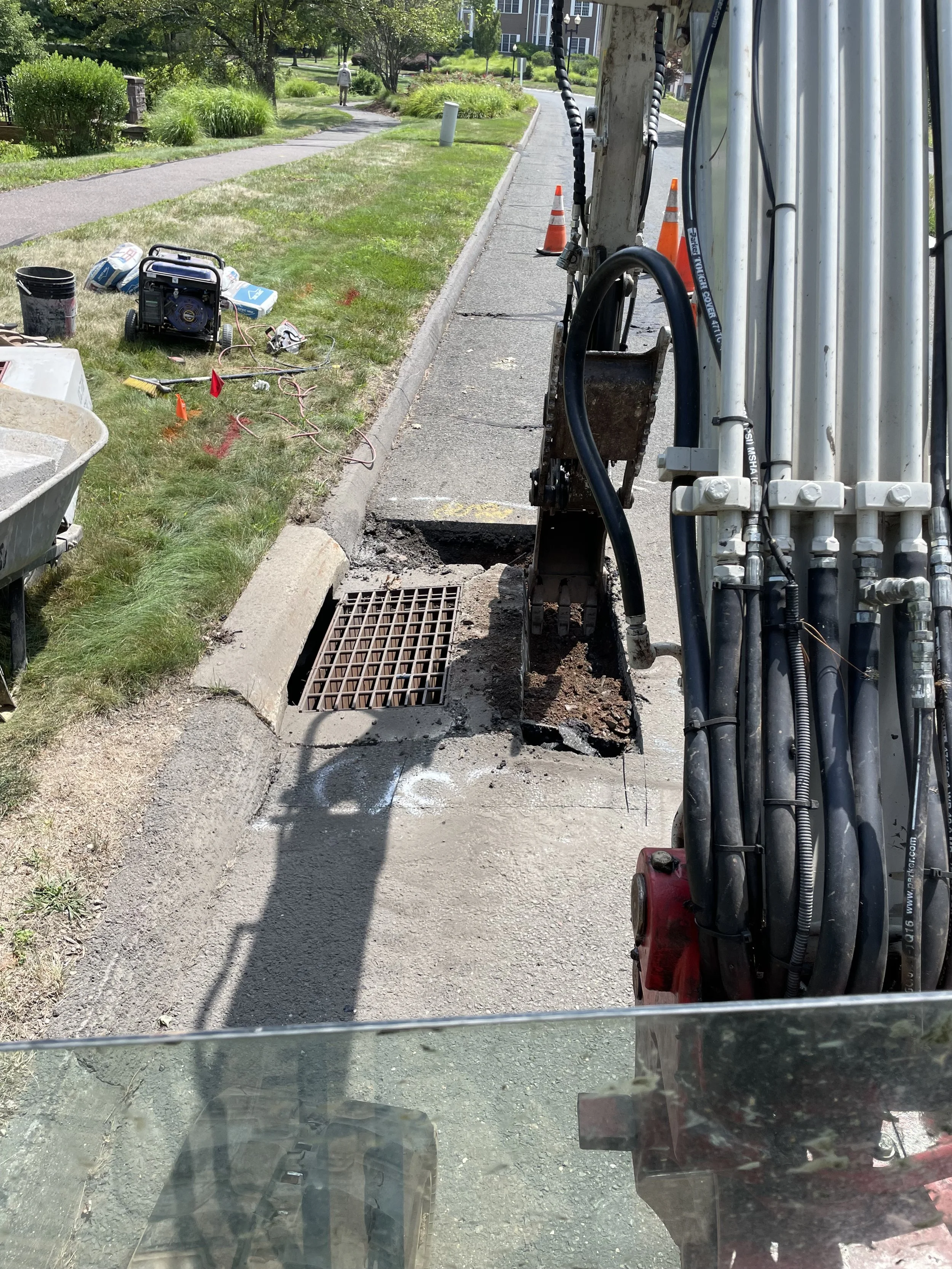 Construction worker operating an excavator to repair or maintain a water drain on a sidewalk.