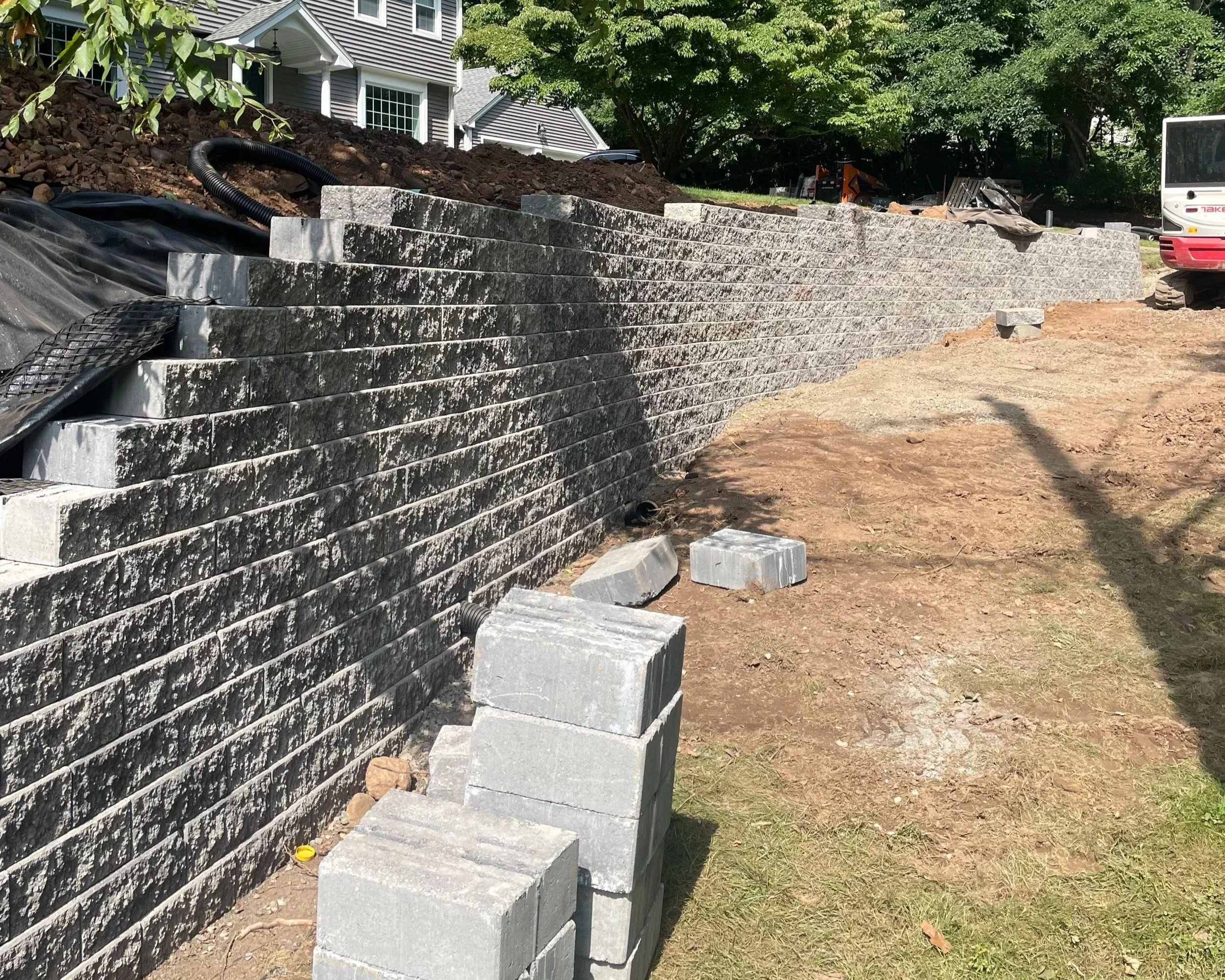 Construction site with a long stone brick retaining wall under construction, with loose bricks and construction equipment around.