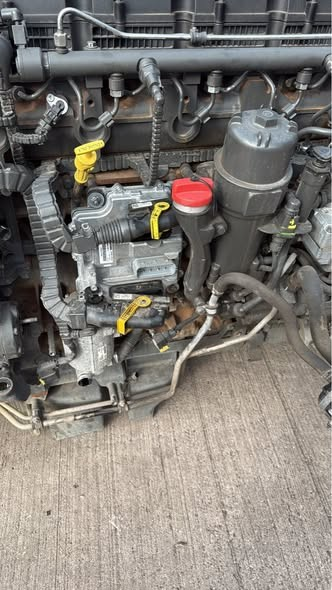 Close-up of an engine with various hoses, caps, and components, including a red cap and yellow levers.