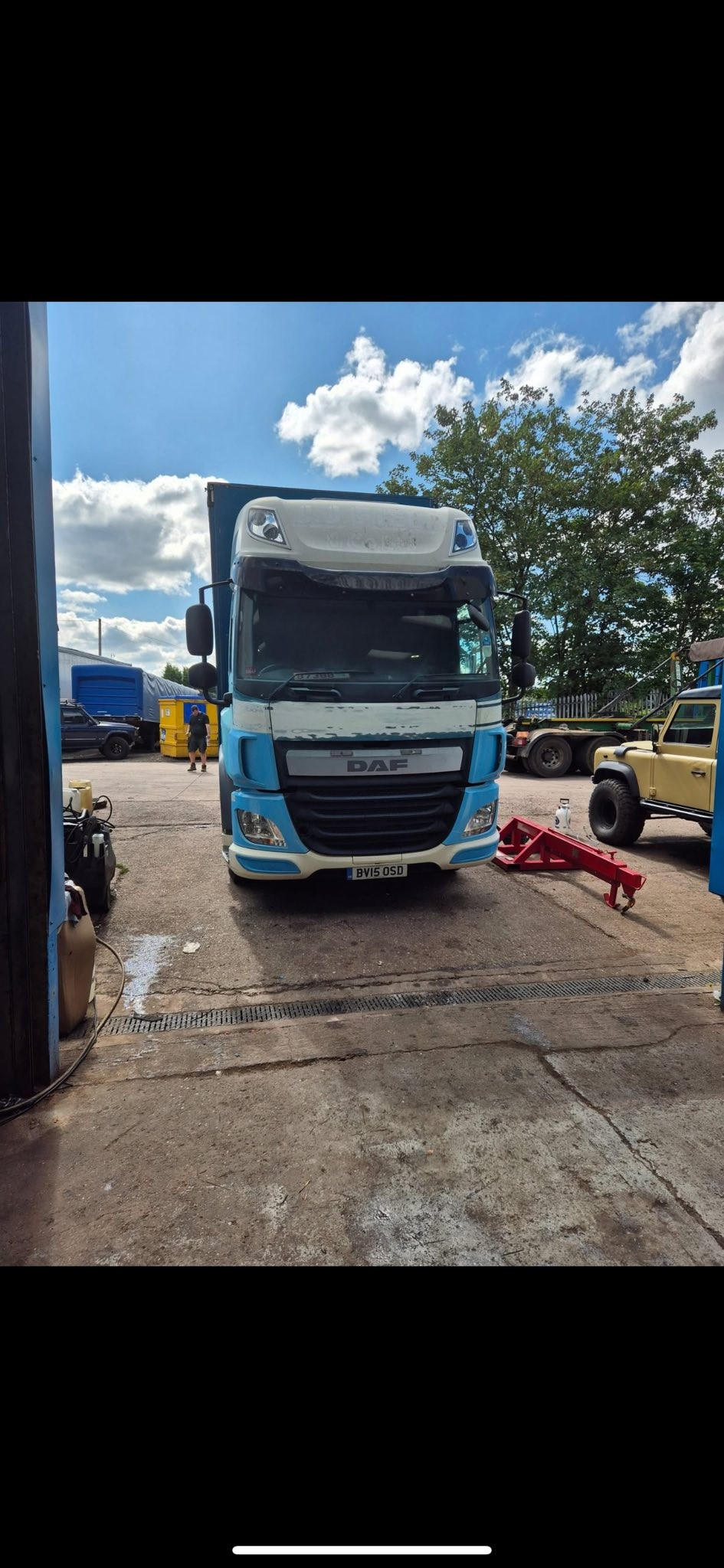 Front view of a blue and white DAF truck in a garage or workshop area.
