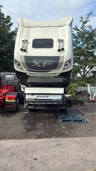 Front view of a white DAF XF semi-truck cab with the grille and logo visible, propped up on a stand in an outdoor parking lot.