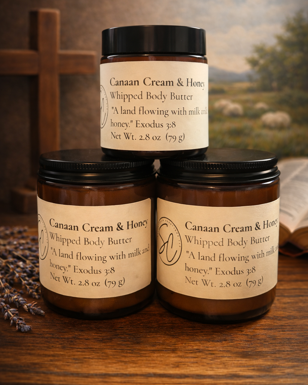 Three amber jars of Canaan Cream & Honey Whipped Body Butter stacked on a wooden surface, featuring Exodus 3:8 on cream labels.