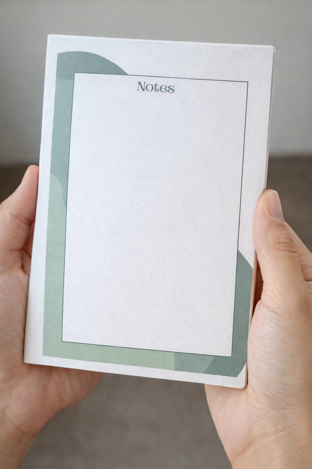 Hands holding a 5x7 minimalist notepad with green corner accents and open writing space.