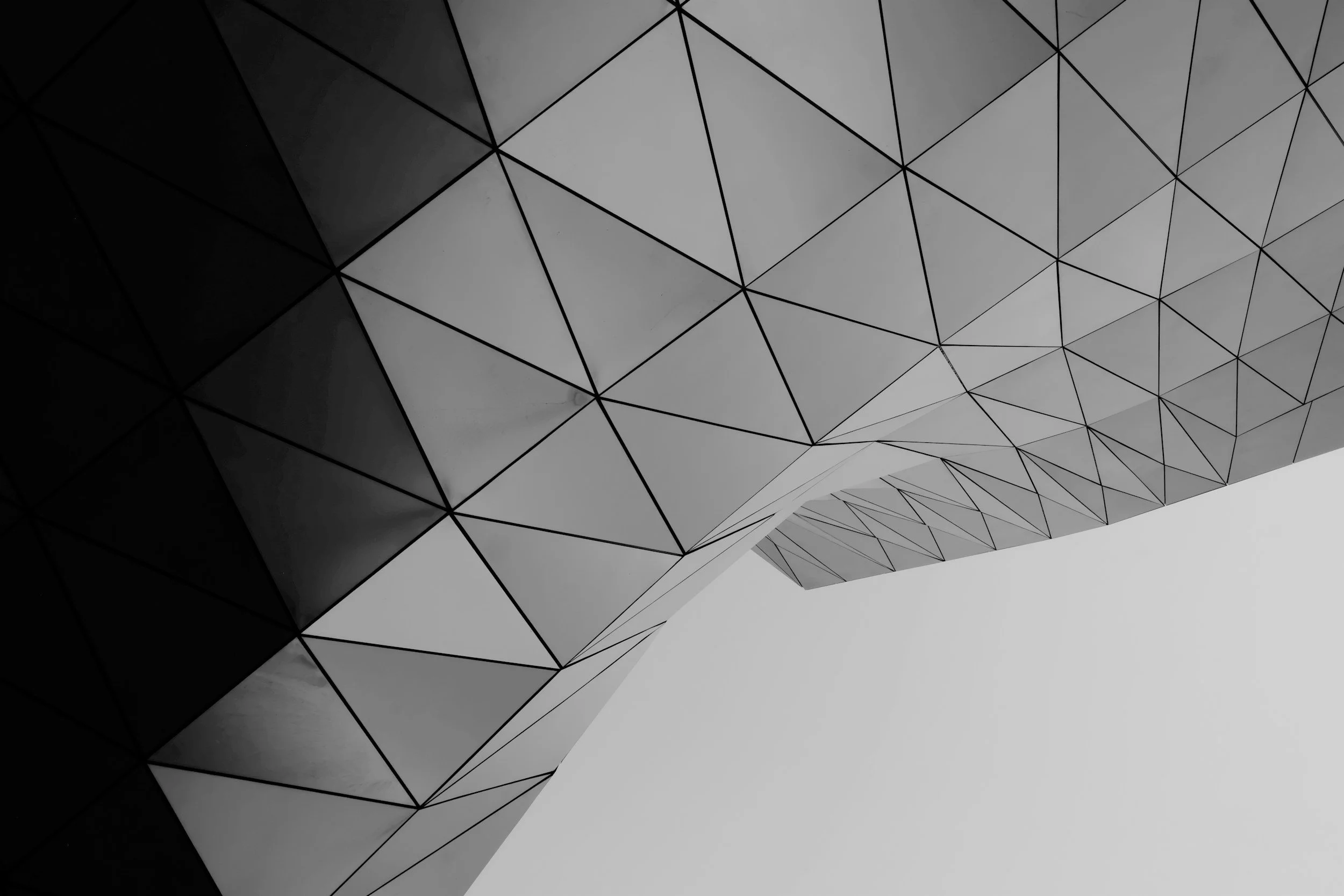 Close-up of a modern building with a geometric, triangular pattern on its facade, photographed from below.