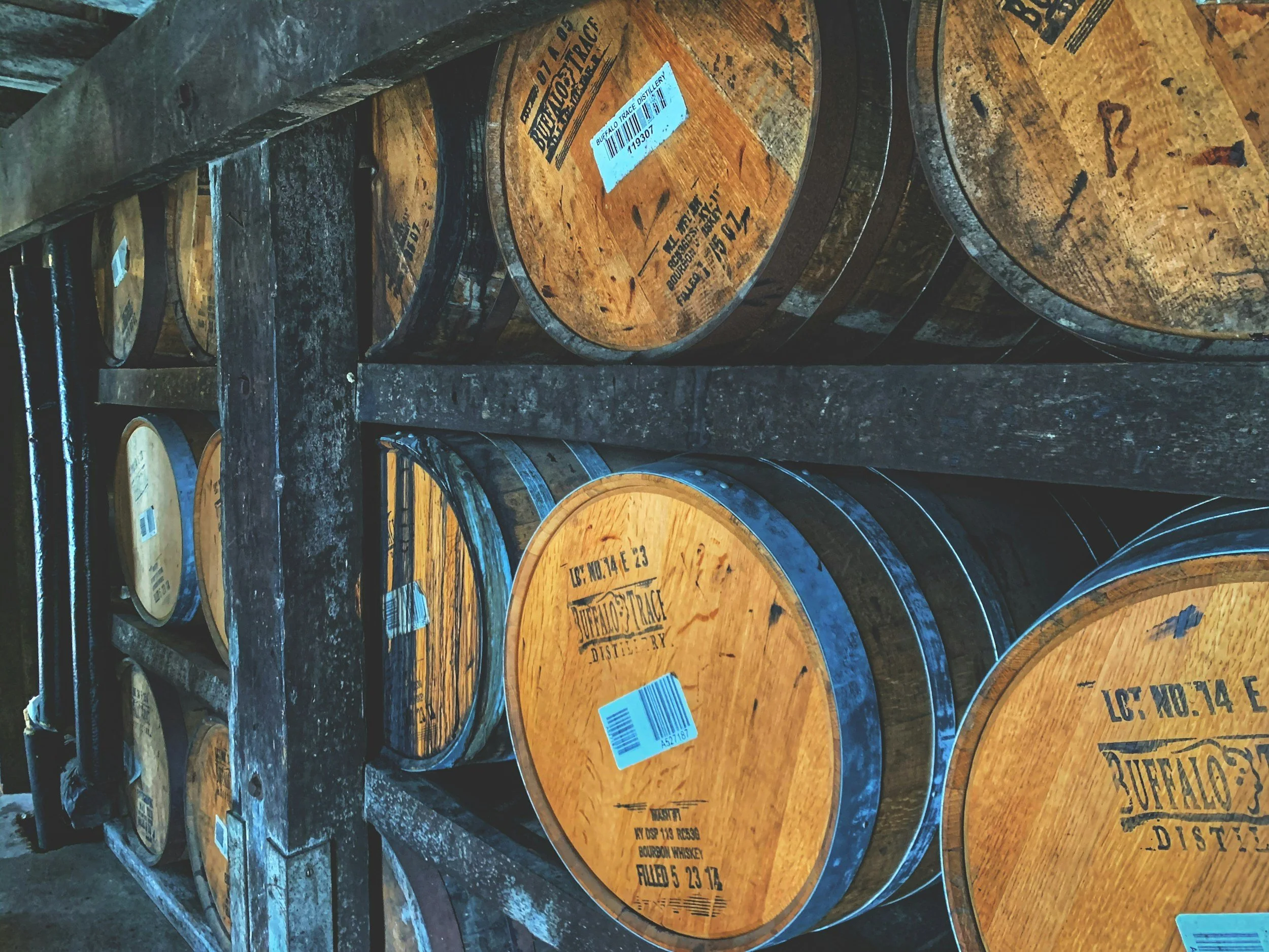 Wooden barrels stacked on metal racks in a warehouse.