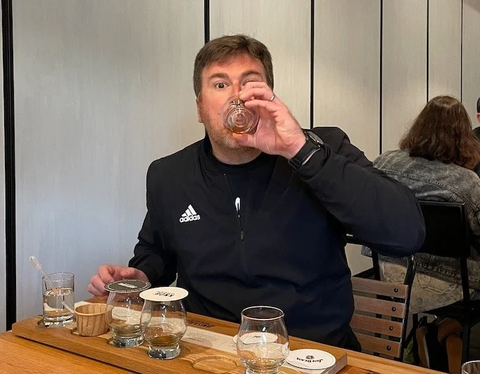 A man wearing a black Adidas jacket drinking from a glass.