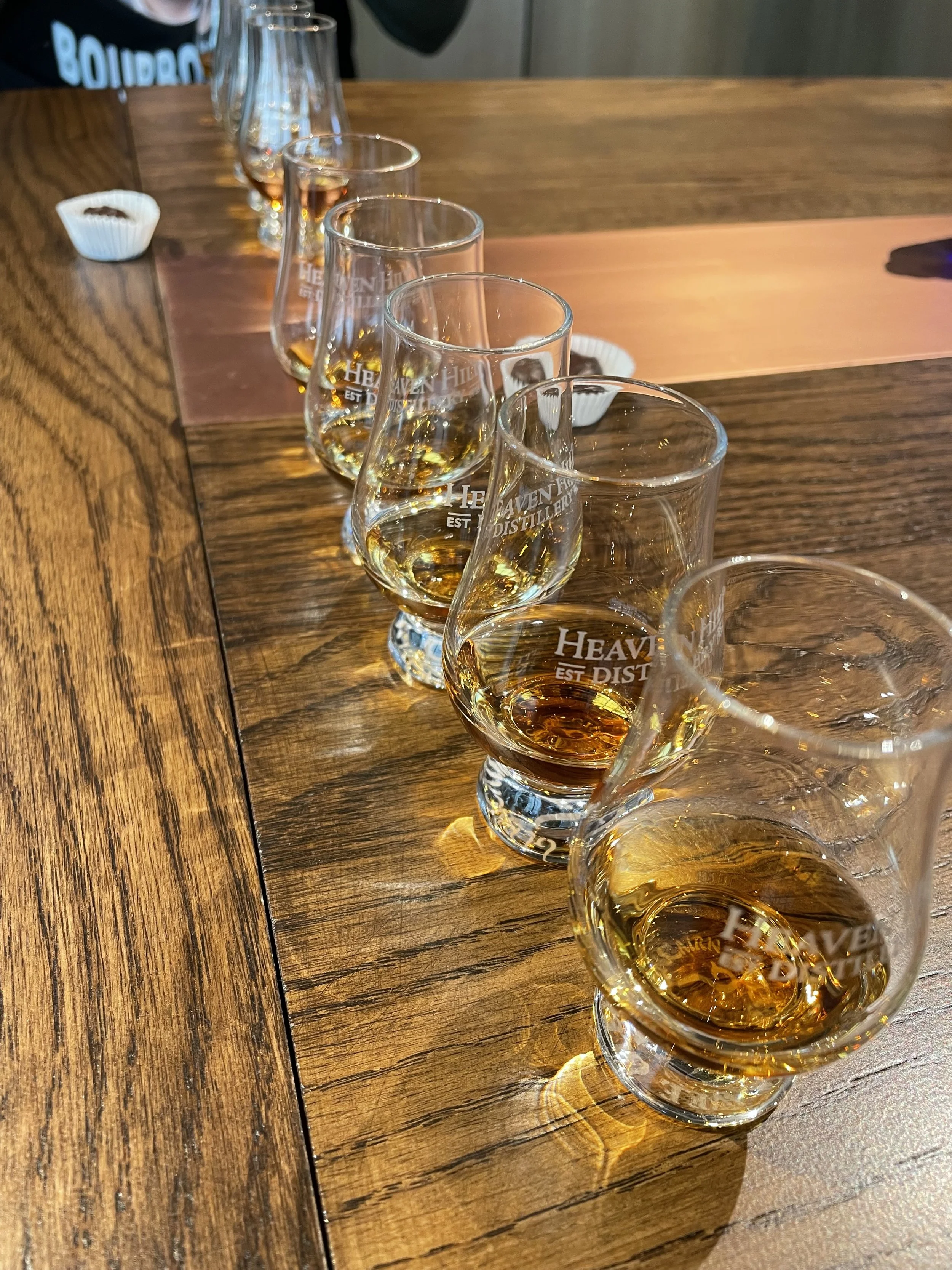 Six Glencairn glasses filled with whiskey arranged on a wooden table.