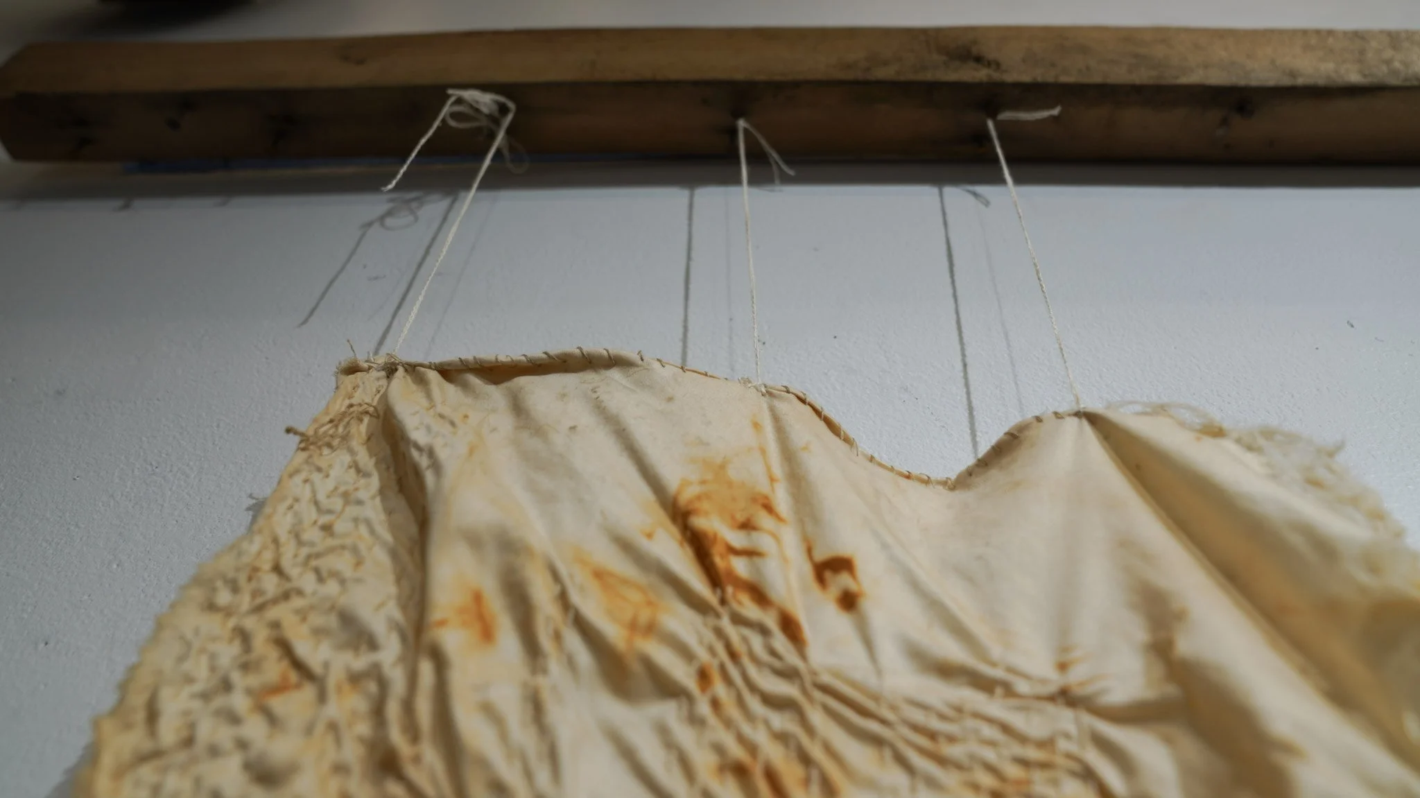 Close-up of a weathered fabric hanging from a piece of wood with white string.