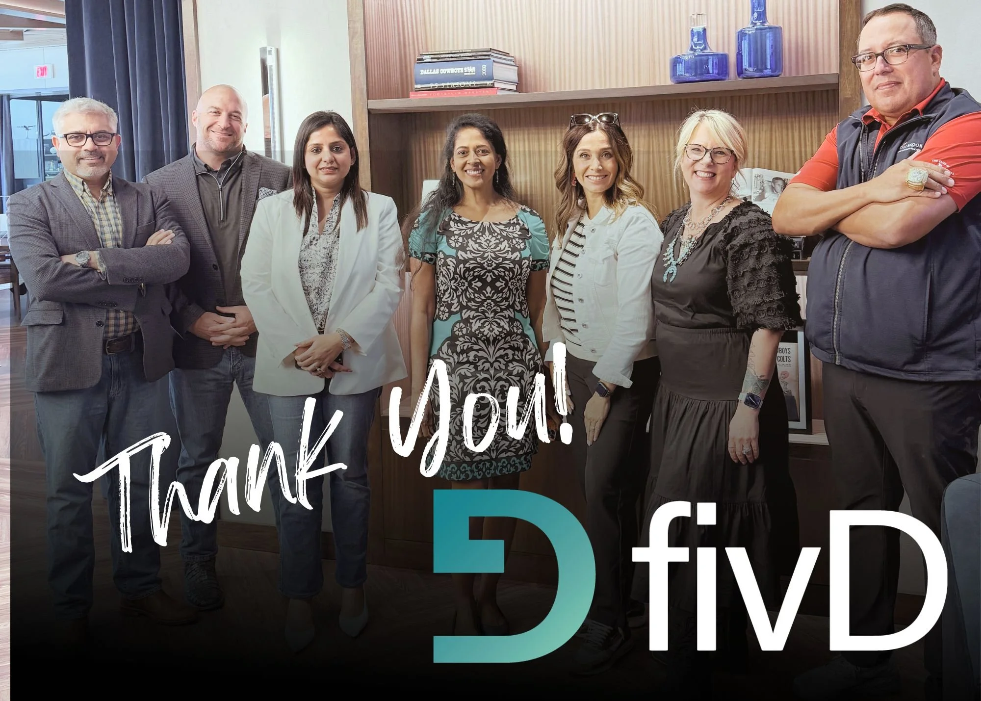A group of eight diverse adults standing together indoors, smiling at the camera. They are in an office setting with wooden shelves, books, and decorative glass bottles in the background. The image includes overlaid text that reads 'Thank You! D TIVD