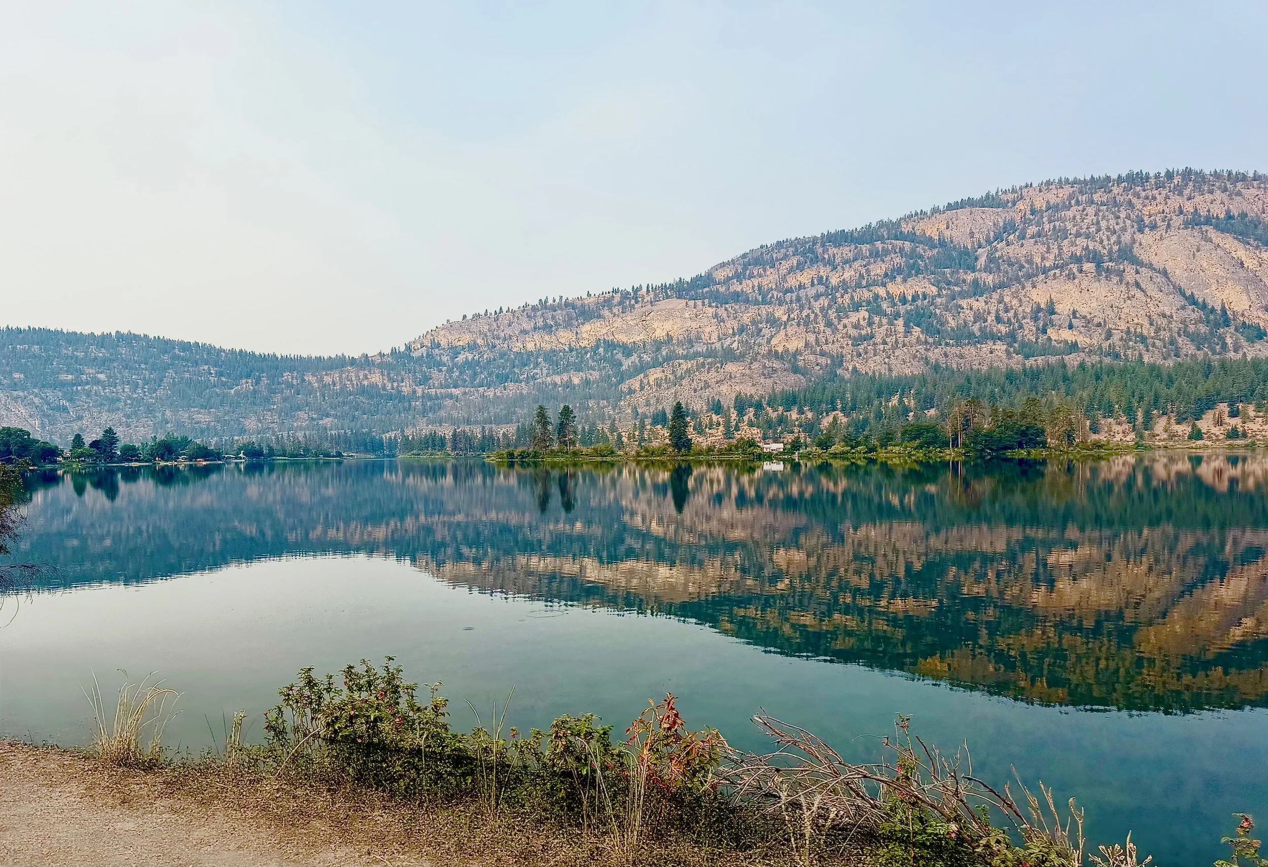 Still water creates a near-perfect reflection of the rugged hills surrounding Skaha Lake.