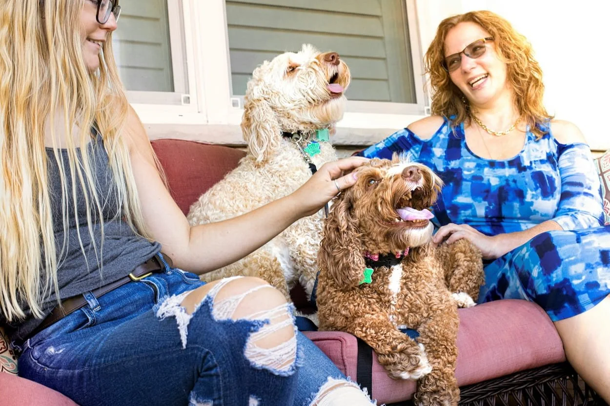 Two women sitting on a porch petting their two happy dogs