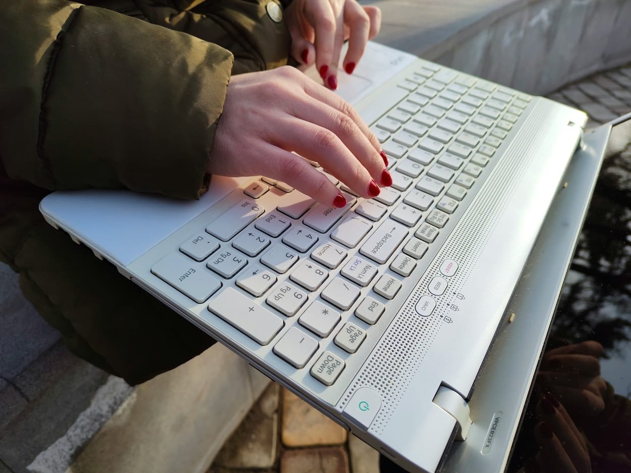 Person typing on a laptop keyboard outdoors