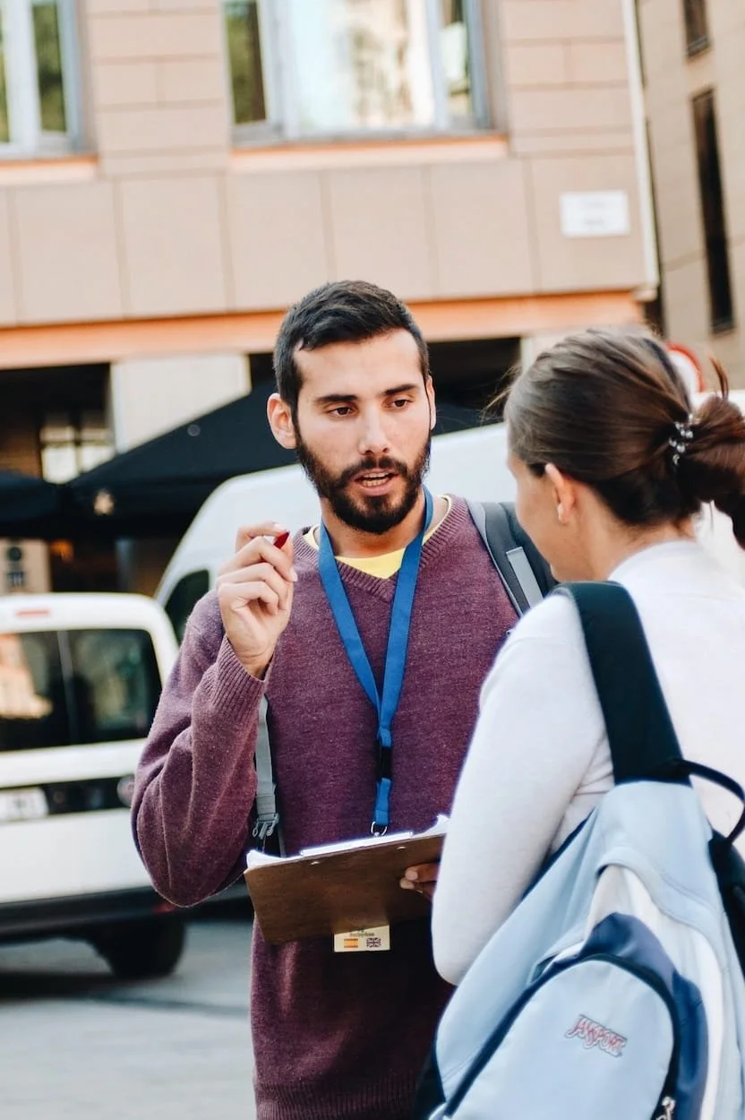 Volunteer with a clipboard speaking to a person on the street