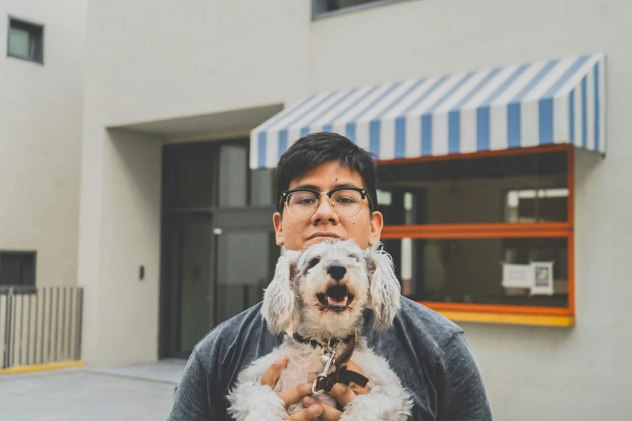 Young man holding a small happy dog in front of a building