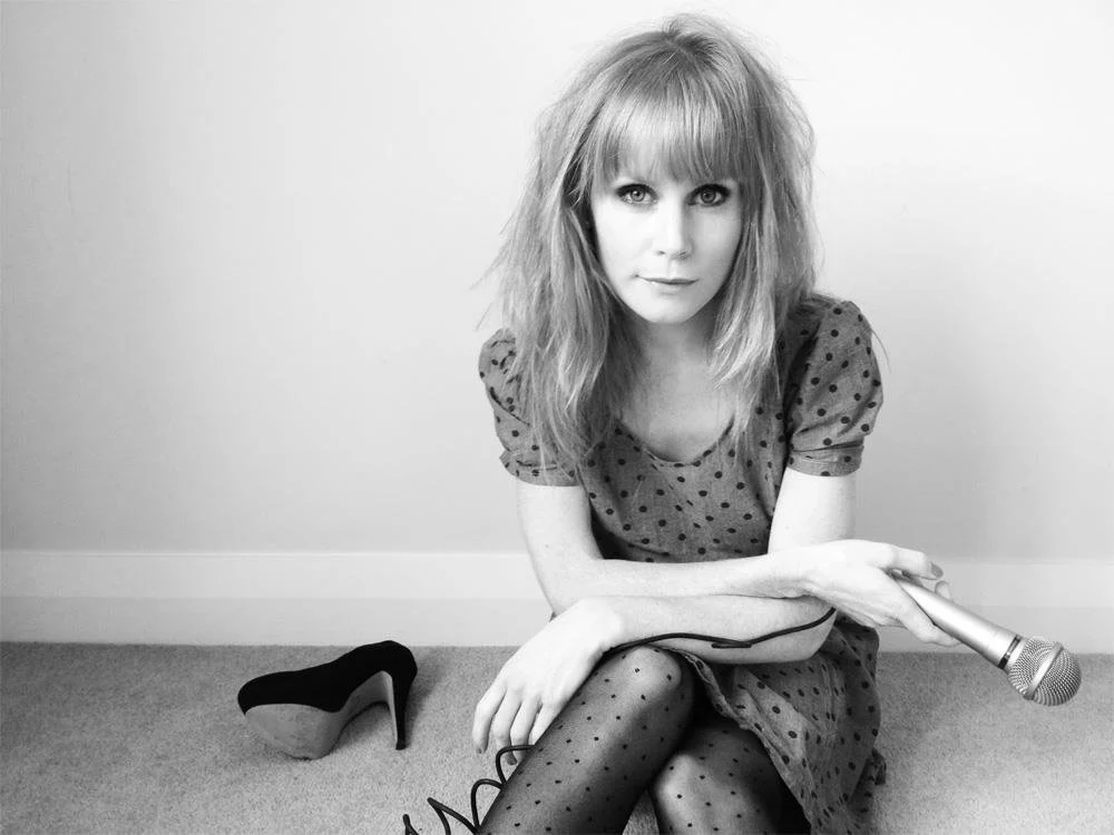 A black and white poster image of Michelle Blundell for the New Zealand production of Eigengrau at Basement Theatre. Michelle has a microphone in one hand and is wearing a polka dot dress and stockings