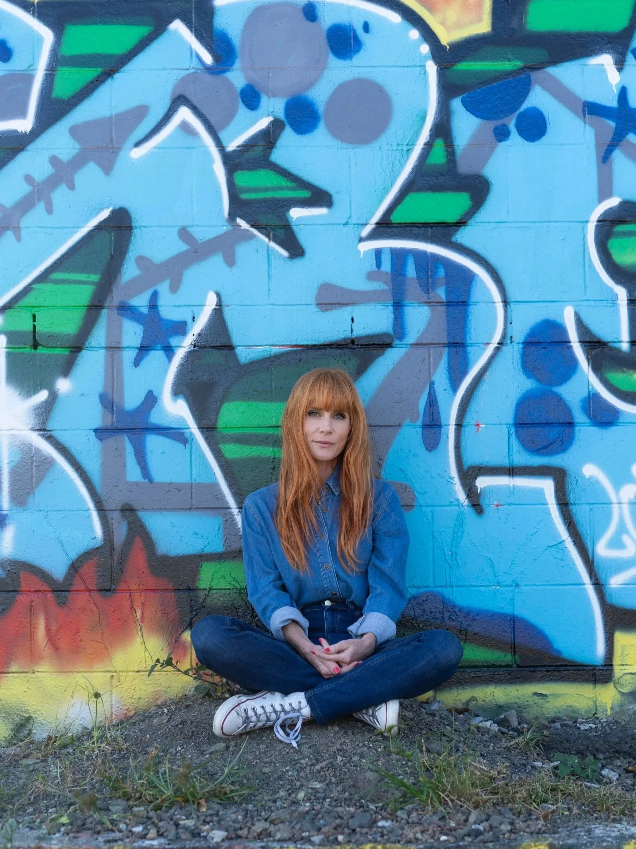 New Zealand actor Michelle Blundell photographed by Emma Cosgrave. She is leaning against a bright blue graffiti wall