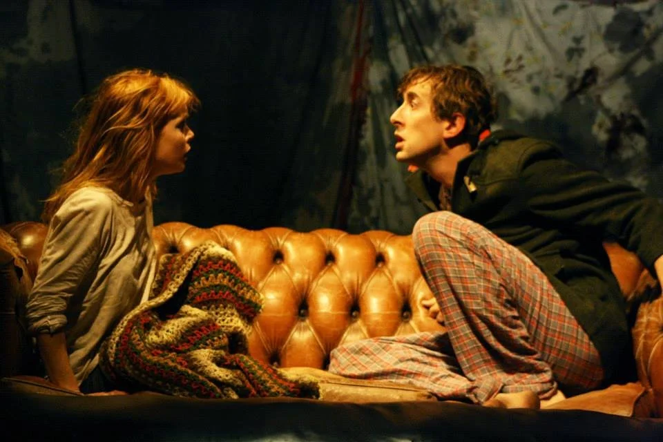 Actors Michelle Blundell and Todd Emerson in a production still from The Pitchfork Disney at Q Theatre. They are facing toward each other on an old leather couch