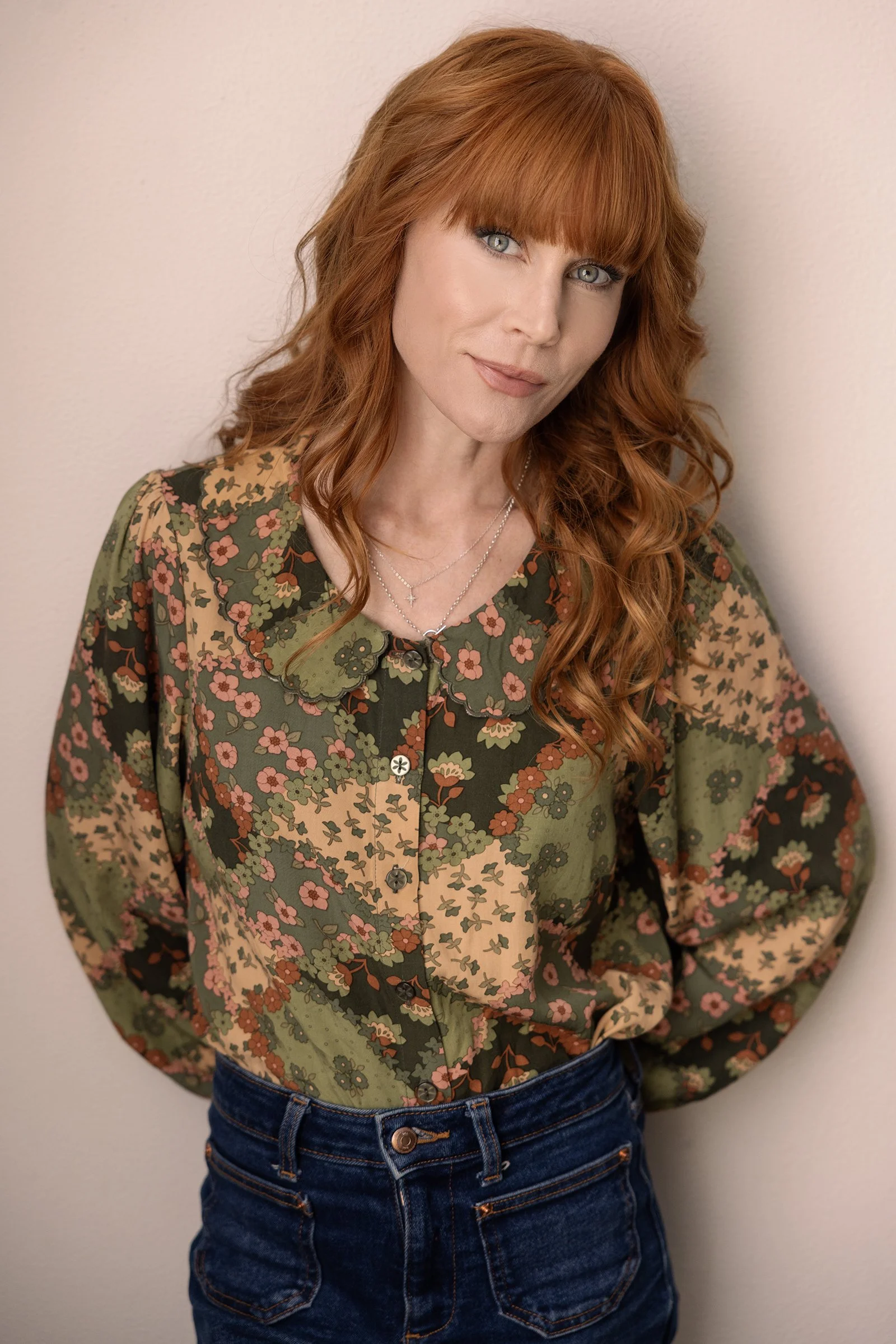 Actor Michelle Blundell leaning against a wall taken by Andi Crown Photography. She is wearing a floral patterned top and denim jeans